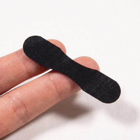 A single nasal strip resting across two fingertips, showing how small it is